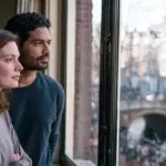 Couple standing close together at a window, one partner turned slightly away from the other